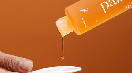 Close up image of a bottle of orange skincare liquid, Pai Bright Now Exfoliating Toner, being poured onto a reusable cotton pad