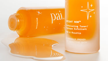 Close up image of two bottles of orange skincare liquid, Pai Bright Now Exfoliating Toner, one on its side, left, and the base of the second, right